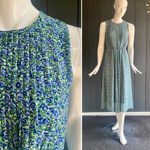 Könnte beinhalten: Ein ärmelloses, plissiertes Kleid mit einem blauen und grünen Blumendruck. Das Kleid hat einen runden Ausschnitt und einen taillierten Oberteil. Das Kleid wird auf einer Schaufensterpuppe gezeigt.