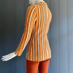 May include: A striped long-sleeved shirt with brown, white, and orange stripes. The shirt is worn with matching brown pants.