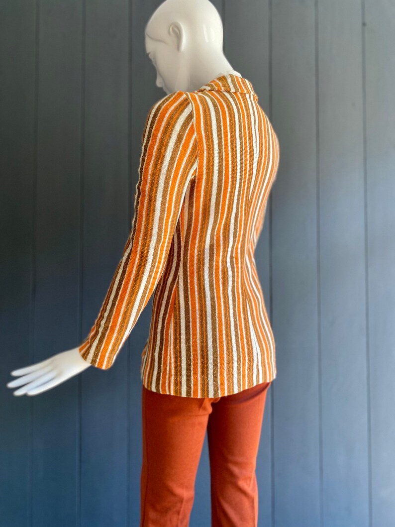 May include: A striped long-sleeved shirt with brown, white, and orange stripes. The shirt is worn with matching brown pants.