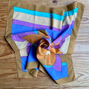 May include: A brown silk scarf with a floral design in shades of orange, purple, and blue. The scarf has a striped border in beige, purple, blue, and turquoise. The text "JACQUES FATH" is visible on the scarf.