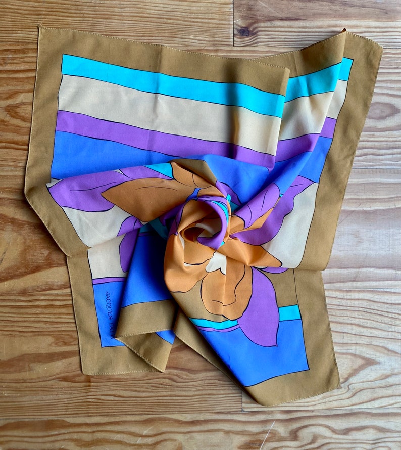 May include: A brown silk scarf with a floral design in shades of orange, purple, and blue. The scarf has a striped border in beige, purple, blue, and turquoise. The text "JACQUES FATH" is visible on the scarf.