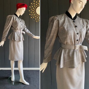 May include: A gray and white plaid skirt suit with a peplum top and a black velvet collar. The suit has a fitted skirt and a long-sleeved jacket with puffed shoulders. The jacket has a button closure and a belt.