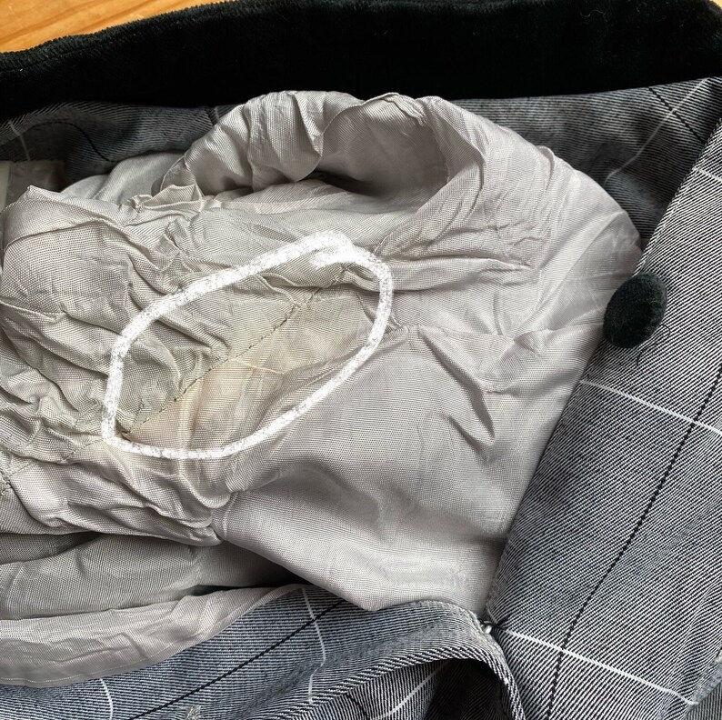 May include: Close-up of the inside of a gray and black plaid blazer. The lining is a light gray color and has a small, light brown stain.