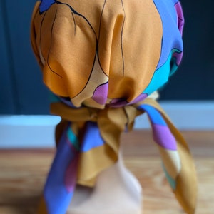 May include: A brown and blue patterned headscarf with a floral design. The scarf is tied around a mannequin's head.