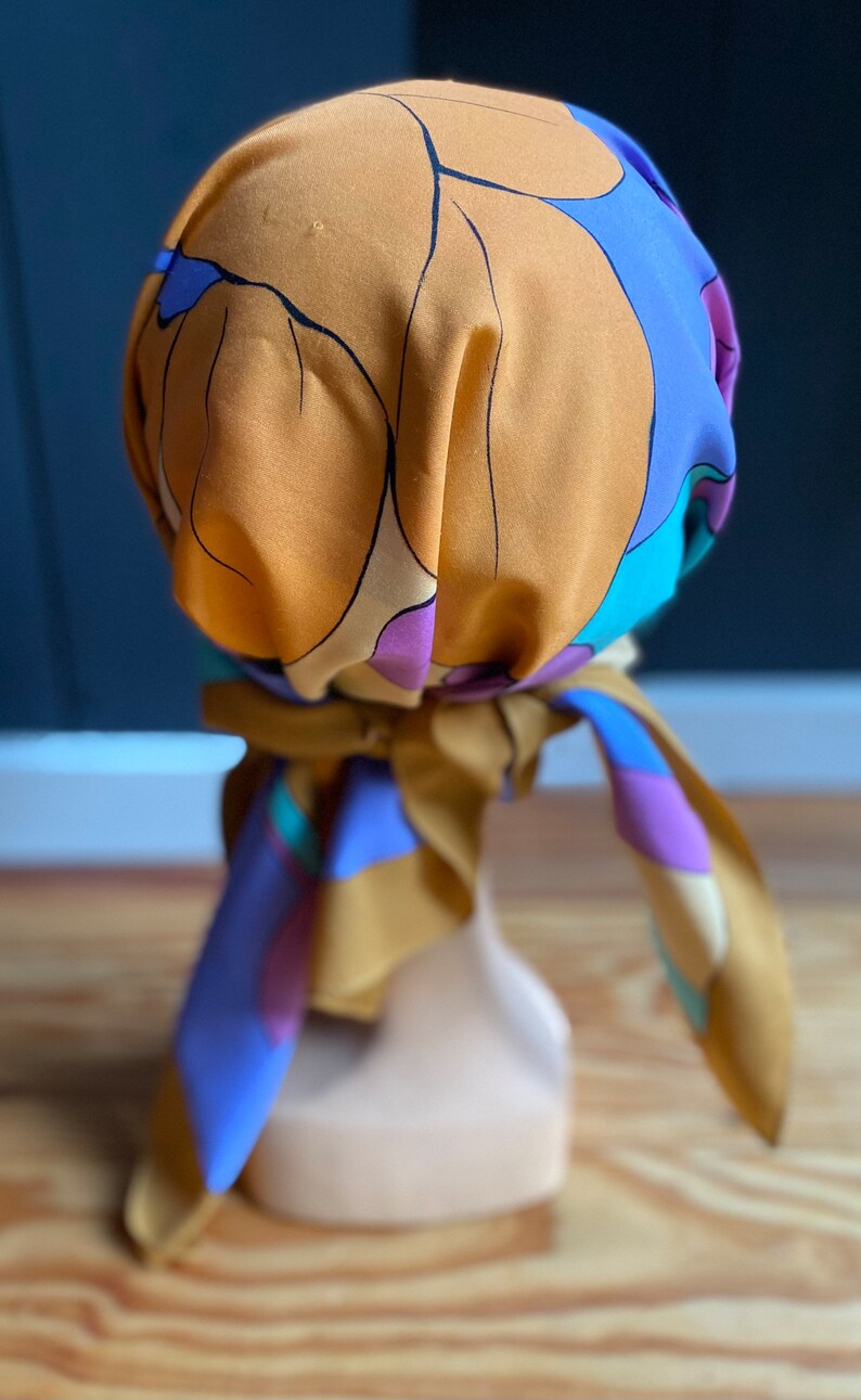 May include: A brown and blue patterned headscarf with a floral design. The scarf is tied around a mannequin's head.