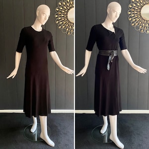 Peut inclure: Une robe midi noire avec un décolleté légèrement asymétrique. La robe est présentée sur un mannequin avec une ceinture en cuir noir.