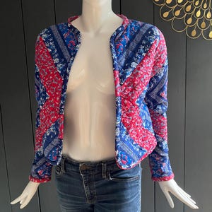 Peut inclure: Une veste matelassée avec un motif paisley bleu et rouge. La veste a un col montant et des manches longues.