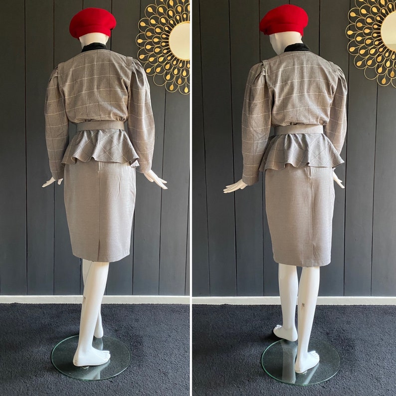 May include: A gray plaid skirt suit with a peplum top and a red beret. The suit is on a mannequin.