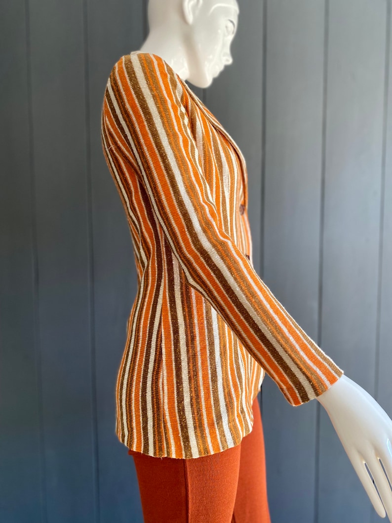 May include: A striped blazer with brown, orange, and white stripes. The blazer has a single button closure and long sleeves.