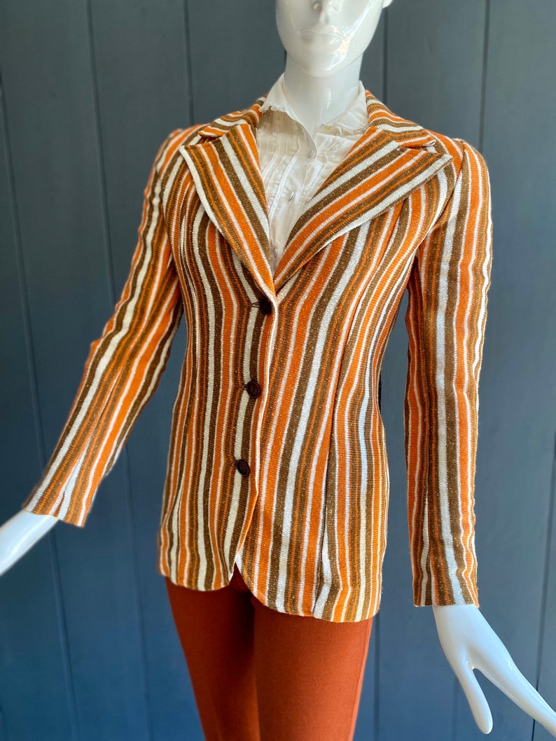 May include: A striped blazer with brown, orange, and white stripes. The blazer has a single button closure and long sleeves.