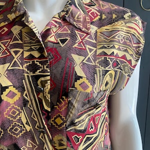 May include: A short-sleeved button-down shirt with a geometric pattern in shades of burgundy, yellow, black, and gray. The shirt features a collared neckline and a single chest pocket. The fabric has a vintage aesthetic.