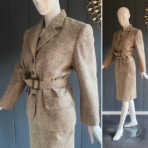 May include: A vintage tweed suit featuring a blazer with a belted waist and a matching pencil skirt. The suit is a mix of brown and tan tones, with a textured fabric. The blazer has a notched collar, button closure, and pockets. The skirt is knee-length.