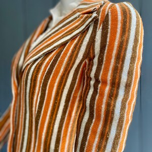 May include: A striped knit blazer with a brown, white, and orange color scheme. The blazer has a collar and long sleeves.
