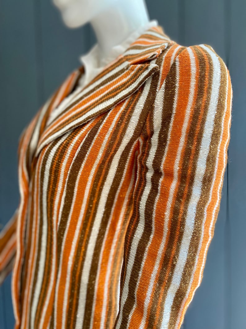 May include: A striped knit blazer with a brown, white, and orange color scheme. The blazer has a collar and long sleeves.