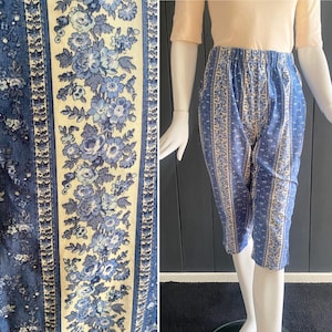 May include: Blue and cream floral print capri pants. The capris feature a repeating floral pattern in shades of blue and cream. The pants have an elastic waistband and are displayed on a mannequin. The fabric has a soft, lightweight appearance.