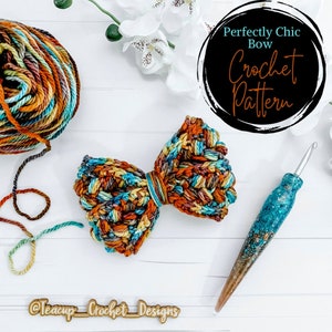 May include: A crochet bow with a multi-colored yarn in shades of brown, orange, blue, and teal. The bow is on a white wooden surface with a ball of yarn and a crochet hook. The text "Perfectly Chic Bow Crochet Pattern" is in a black circle with a white outline. The text "@Teacup_Crochet_Designs" is on a wooden sign.