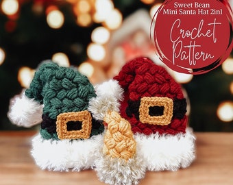 May include: Two crocheted mini Santa hats, one red and one green, with white fur trim and black belts. The hats are on a wooden surface with a blurred Christmas tree background. The text "Sweet Bean Mini Santa Hat 2in1 Crochet Pattern" is visible in the top right corner.