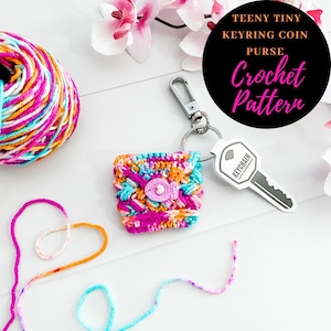 May include: A colorful crocheted coin purse with a heart-shaped button, attached to a silver keychain with a key. The purse is on a white surface with yarn in the background. The text "TEENY TINY KEYRING COIN PURSE Crochet Pattern" is in a black circle.