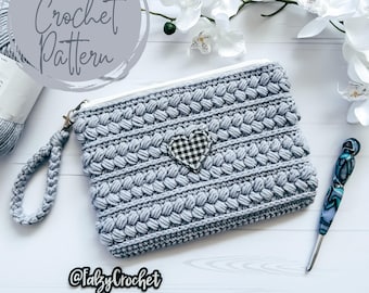 Op de afbeelding: Een grijze gehaakte ritsbeurs met een zwart-wit geblokt hart-applicatie. De beurs heeft een gehaakte band en is gelabeld "Perfectly Chic" Ritsbeurs/Clutch Haakpatroon @TalzyCrochet.