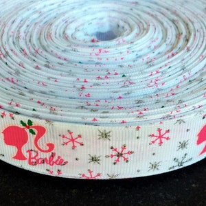 Pu&ograve; includere: Nastro bianco con una silhouette rosa di Barbie e fiocchi di neve. Il nastro ha una finitura glitter argentata e le parole "Barbie" sono stampate sul nastro.