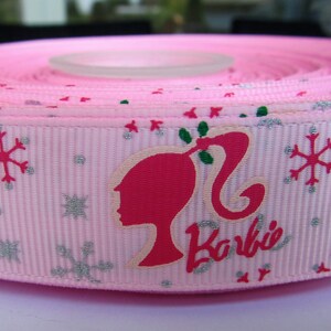 Pu&ograve; includere: Nastro rosa con un motivo a fiocco di neve bianco e una silhouette rosa di Barbie con la parola "Barbie" in lettere argentate scintillanti.