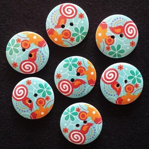 Könnte beinhalten: Sieben Holz-Knöpfe mit türkisfarbenem Hintergrund und bunten floralen und spiralförmigen Designs. Die Knöpfe haben jeweils zwei Löcher.