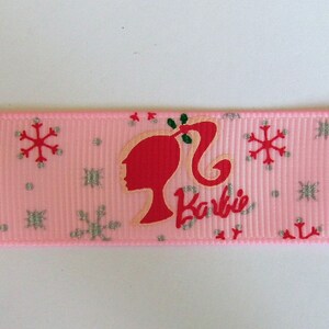 Pu&ograve; includere: Nastro rosa con un motivo a fiocco di neve bianco e un'immagine ripetuta di una silhouette di Barbie rossa con la parola "Barbie" in lettere rosse.