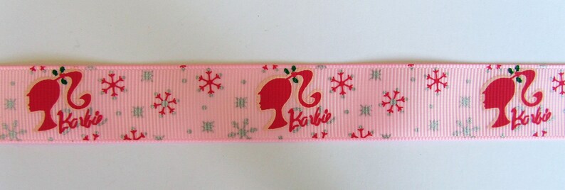 Pu&ograve; includere: Nastro rosa con un motivo a fiocco di neve bianco e un'immagine ripetuta di una silhouette di Barbie rossa con la parola "Barbie" in lettere rosse.