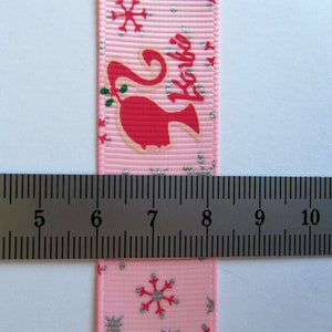 Pu&ograve; includere: Nastro rosa con un motivo a fiocco di neve argentato e la scritta "Barbie" stampata su di esso. Il nastro viene misurato con un righello, mostrando che &egrave; largo 2,5 cm.