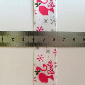 Pu&ograve; includere: Nastro bianco con un motivo di fiocchi di neve argentati glitterati. Il nastro presenta una silhouette rosa di Barbie con la parola "Barbie" stampata in bianco.