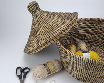 May include: A woven basket with a lid, filled with yarn balls and a crochet hook. There are also scissors and a crocheted circle on a white surface.