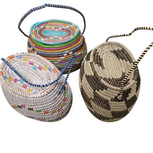 May include: Three woven baskets with handles. The baskets are oval shaped and made of natural materials. One basket is white with colourful stripes, another is white with black stripes, and the third is multi-coloured.