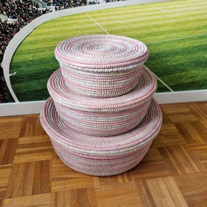 May include: Three pink and white woven baskets stacked on top of each other. The baskets are round and have a lid.