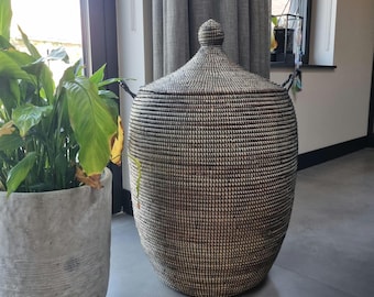 May include: A tall, cylindrical woven basket featuring a dark brown and off-white textured pattern. The basket has a matching conical lid with a small, rounded knob handle at the top and two small side handles for lifting and carrying.