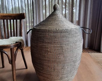 May include: A tall, cylindrical woven basket with a conical lid and two side handles. The basket features a tight, textured weave pattern in alternating shades of dark brown and natural tan, creating a consistent, neutral-toned appearance.