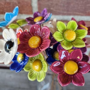 Peut inclure: Un bouquet de fleurs en céramique de différentes couleurs, dont le rouge, le bleu, le vert, le blanc et le jaune. Les fleurs sont disposées dans un vase et ont un aspect rustique et artisanal.