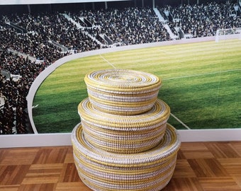 May include: Three round woven baskets with lids, stacked on top of each other. The baskets are white with yellow stripes.