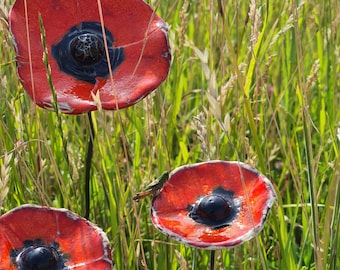 May include: Three ceramic poppy garden stakes with red petals and black centers. The poppies are set in a field of tall green grass and wheat. The red petals have a textured, glazed finish. The stakes are made of dark metal.