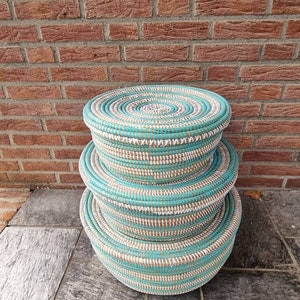 May include: Three round woven baskets with a white and turquoise striped pattern. The baskets are stacked on top of each other.