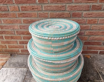 May include: Three round woven baskets with a white and turquoise striped pattern. The baskets are stacked on top of each other.