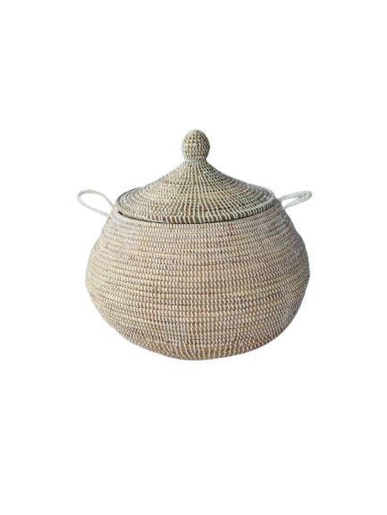 May include: A round, woven basket with a matching conical lid and two small side handles. The basket features a neutral color palette with alternating light beige and off-white horizontal bands, creating a textured, coiled appearance throughout.