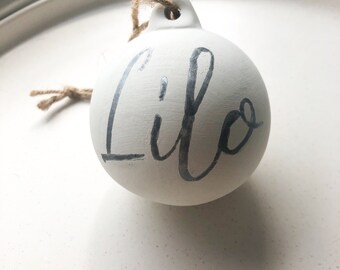 May include: White ceramic ornament with the name "Lilo" written in black calligraphy.