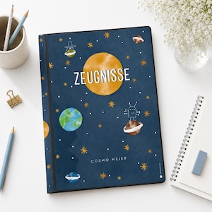 Könnte beinhalten: Ein dunkelblaues Notizbuch mit Weltraum-Design. Das Cover zeigt eine große gelbe Sonne, Planeten, Sterne und das Wort "ZEUGNISSE" in Weiß. Der Name "COSMO MEIER" ist unten aufgedruckt.