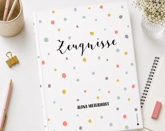 May include: A white notebook with a pastel polka dot design. The word "Zeugnisse" is written in black script on the cover, with the name "ALINA MEIERHOFF" below. The notebook is on a white surface with stationery items.