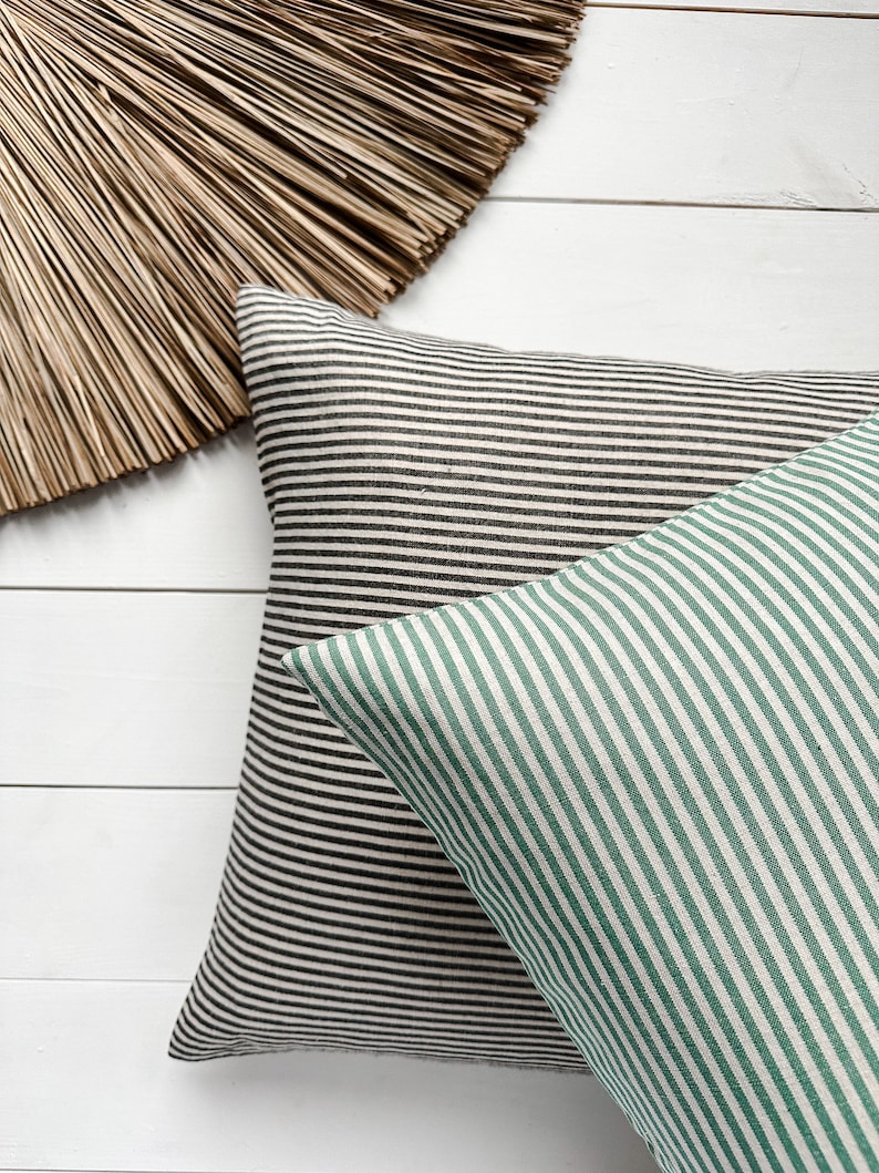 May include: Two striped cushion covers, one black and white, and one green and white, on a white wooden surface.