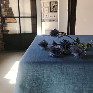 May include: A blue linen tablecloth with a bouquet of purple thistle flowers on top.