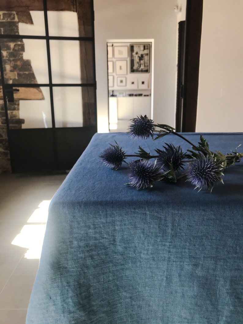 May include: A blue linen tablecloth with a bouquet of purple thistle flowers on top.
