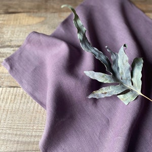 May include: A soft, purple linen kitchen towel with a dried fern leaf on top.