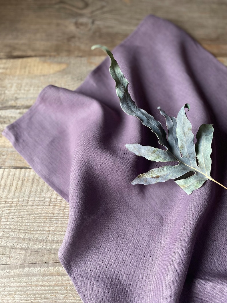 May include: A soft, purple linen kitchen towel with a dried fern leaf on top.