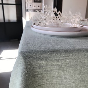 Puede incluir: Un mantel de lino verde claro con un plato blanco encima. El mantel es texturizado y tiene un brillo sutil.
